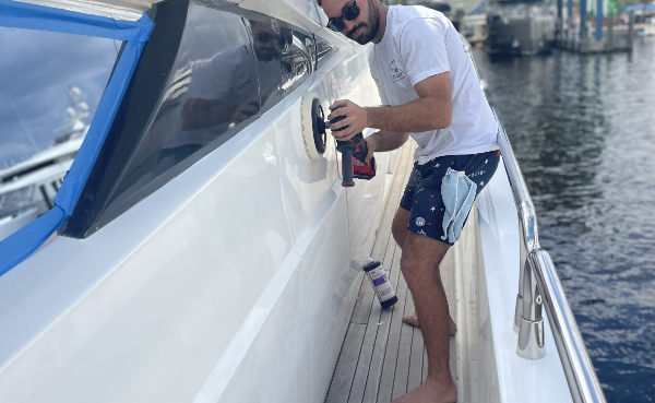 Marine service professional polishing the side of a white yacht at a marina near Gulf Shores, Orange Beach, Foley, and Lillian, Alabama. The vessel is undergoing detailing as part of Oceanside Marine Services’ vessel management program.
